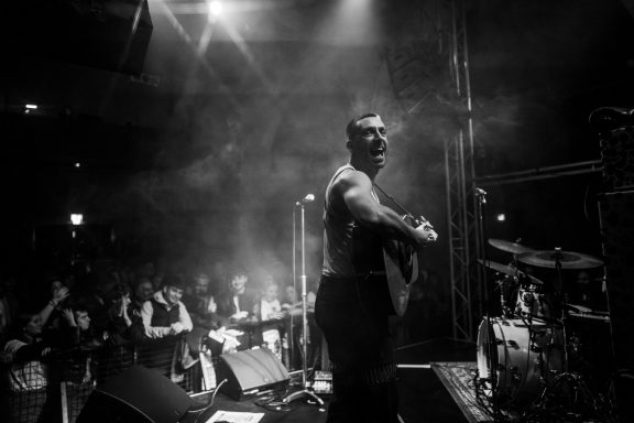 A performer on stage interacting with an audience in a dimly lit venue.