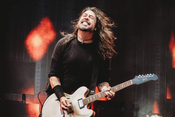 Dave Grohl of Foo Fighters with long hair playing an electric guitar passionately on stage.