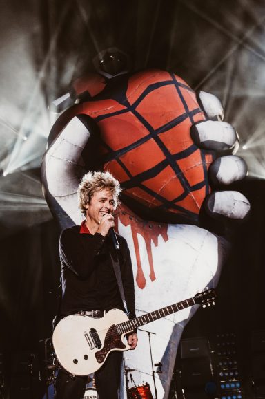 Billie Joe Armstrong of Green Day with a guitar performs in front of a large American idiot artwork backdrop at Wemberly Stadium