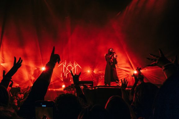 Vessel from sleep token on stage at London O2 Arena with dramatic red lighting and raised hands from the audience.