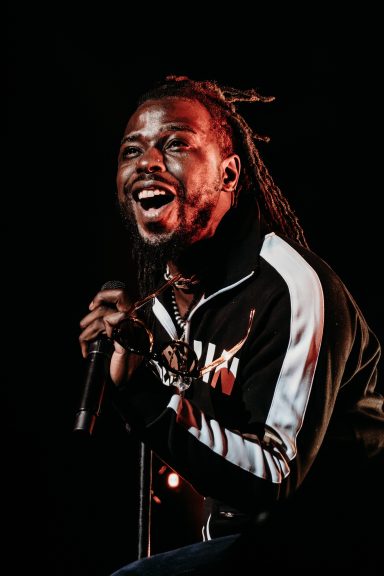 A performer passionately singing into a microphone on stage, with dramatic lighting. Eric from Black Pumas