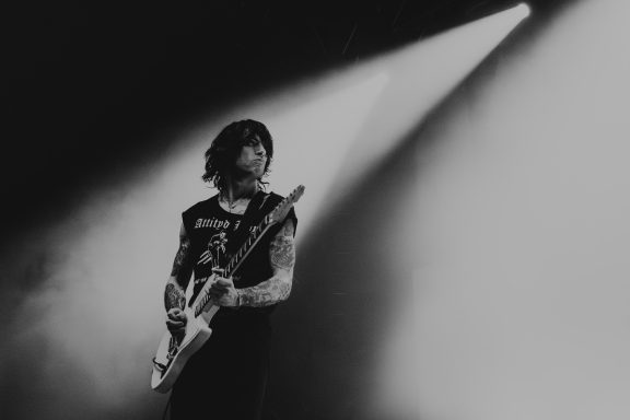 A musician performing on stage with a guitar, illuminated by spotlight. Will Power of Bad nerves